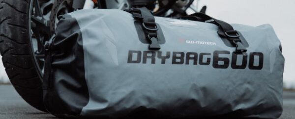 A motorcycle is parked next to a SW-Motech®️ 600 60L Roll-Top Grey/Black Dry Bag.